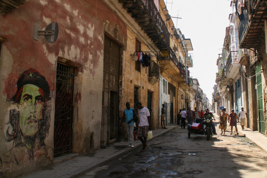 A picture of Che Guevara painted on a foreground wall with people walking the crumbling streets