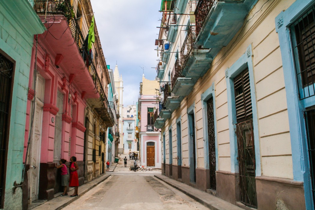 A long shot of a Havana Street. The buildings on the left are painted green and pink and yellow and on the right eggshell with light blue trim