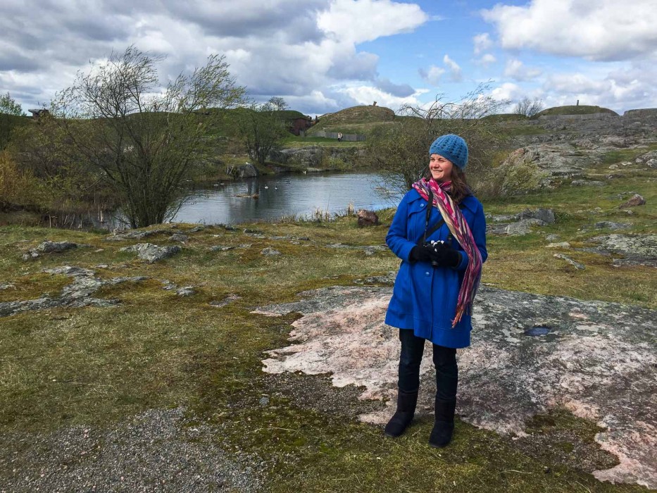 Erin on Suomenlinna island wearing her wool coat with multiple layers beneath, plus hat, scarf, gloves, jeans, and boots. 