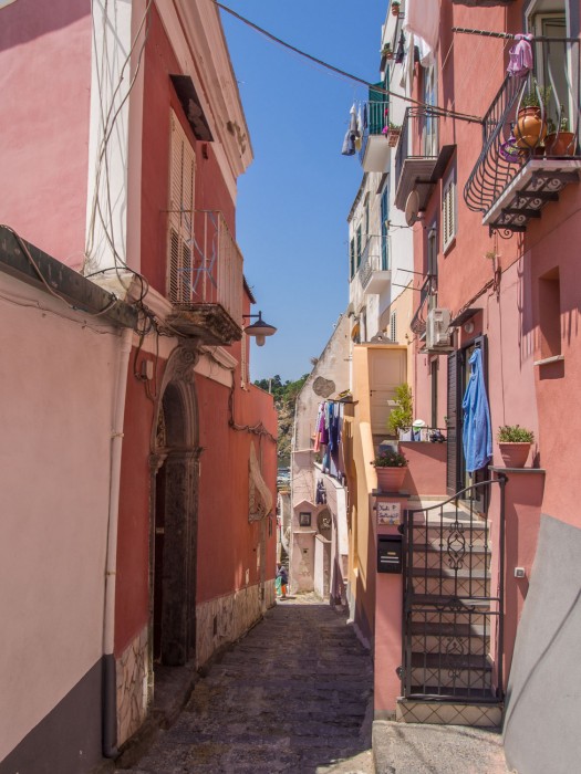 Path inbetween colourful pink buildings to Marina Corricella, Procida island, Italy