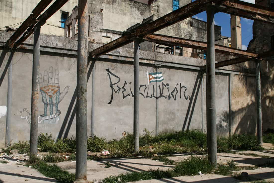 A ruined metal building frame with "Revolucion" painted on the back wall