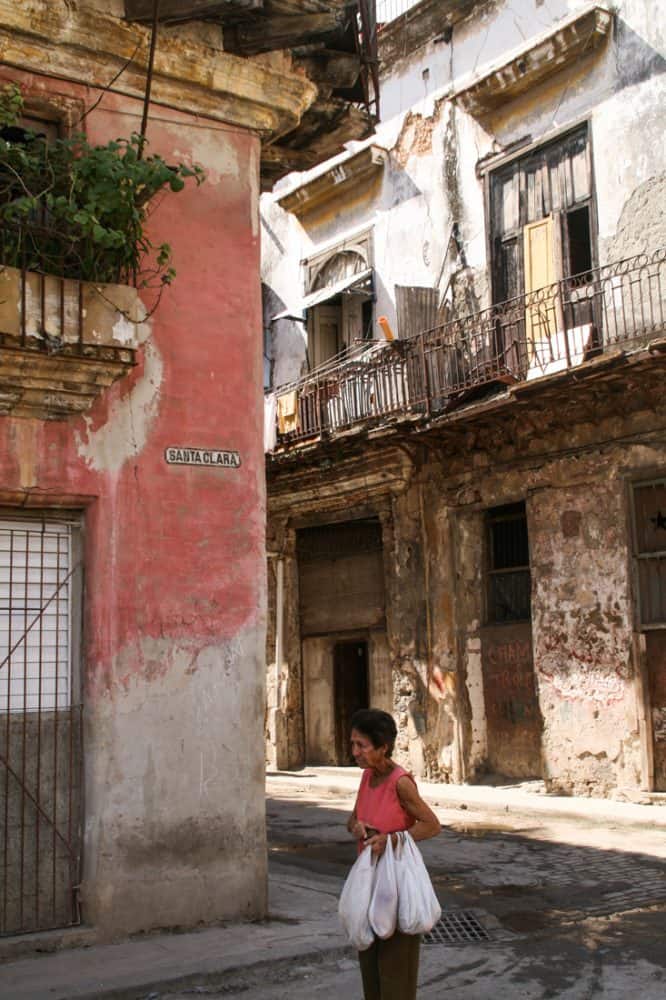 A lady walks with her shopping past a crumbling pink building