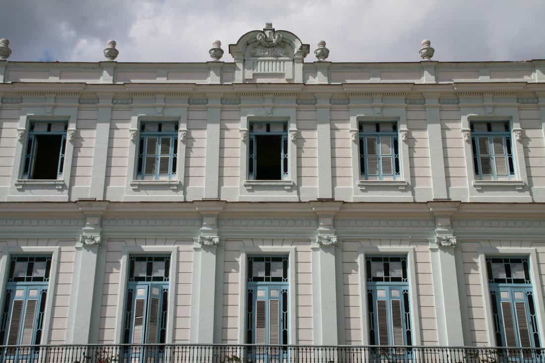 The two-storey façade of a striking white colonial building with light blue trim