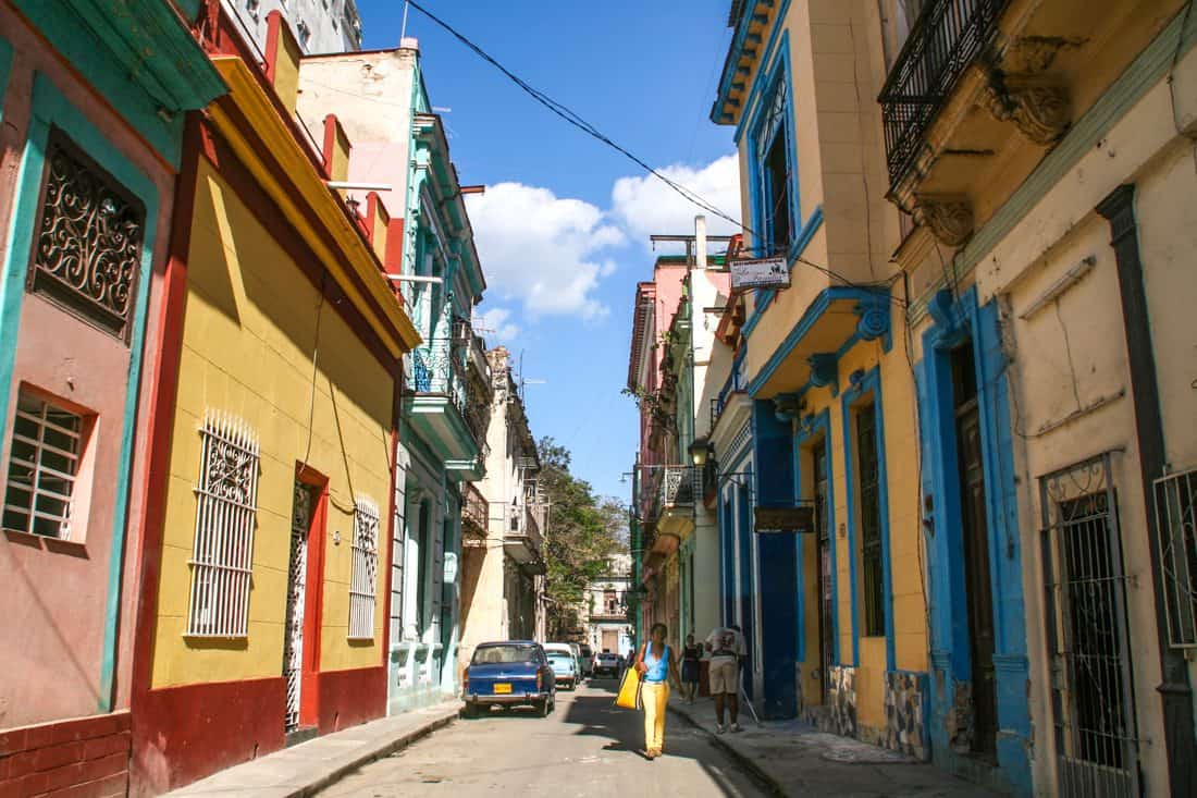 A photo of a street that runs into blue skies, with buildings painted yellow and orange and blue lining both sides