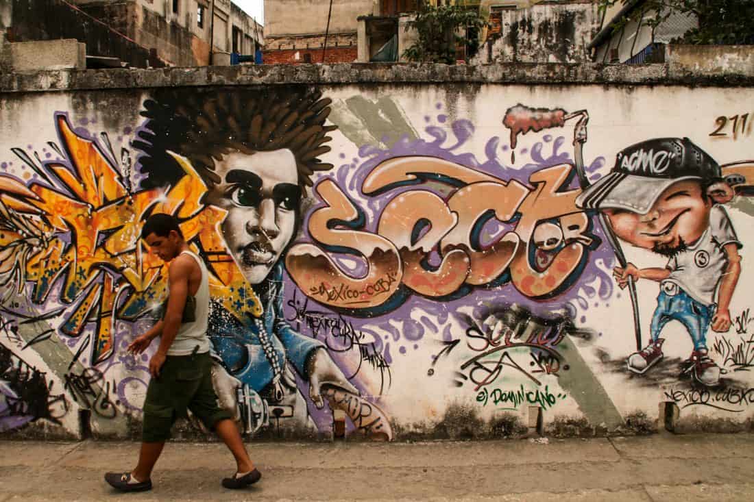 A man walks past a wall painted with Cuban graffiti which features a picture of a man's head and the word 'sect'