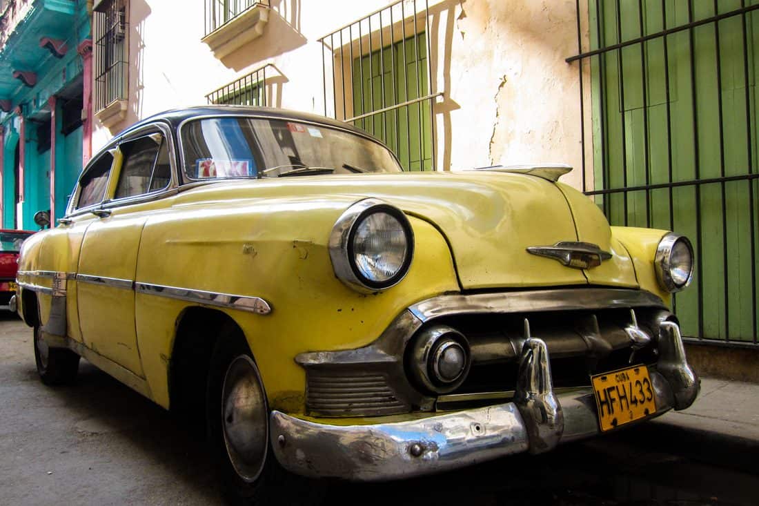 A dirty yellow 1950s Chevrolet sits on the streets of Havana