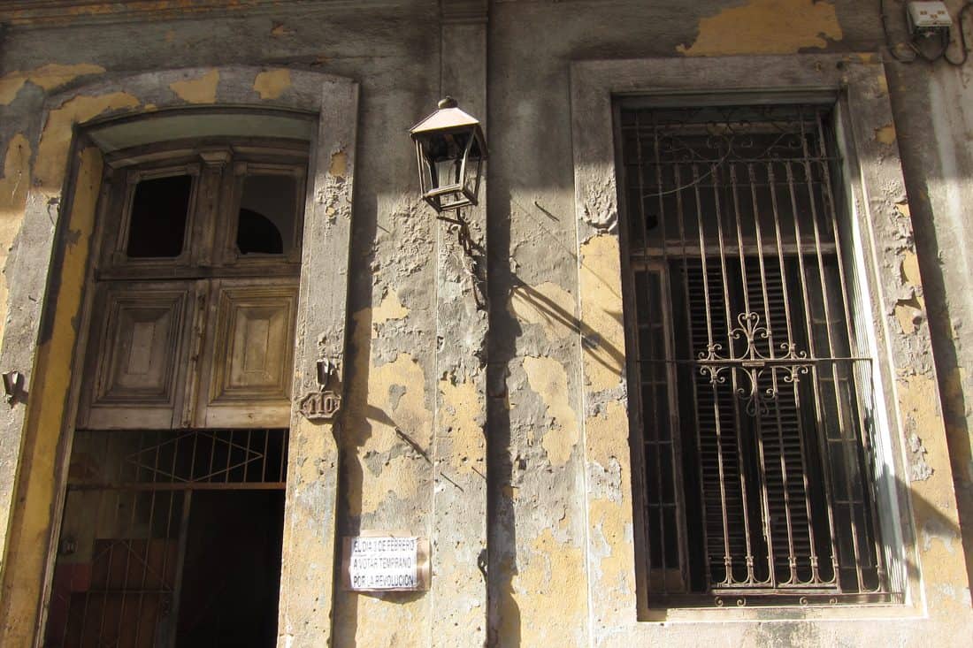 A close up of the front door of an old yellow building that is slowly turning grey