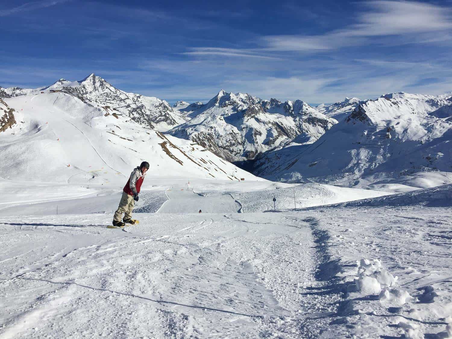 A ski slope with Simon on the left hand side looking back to the camera with the alps in the background