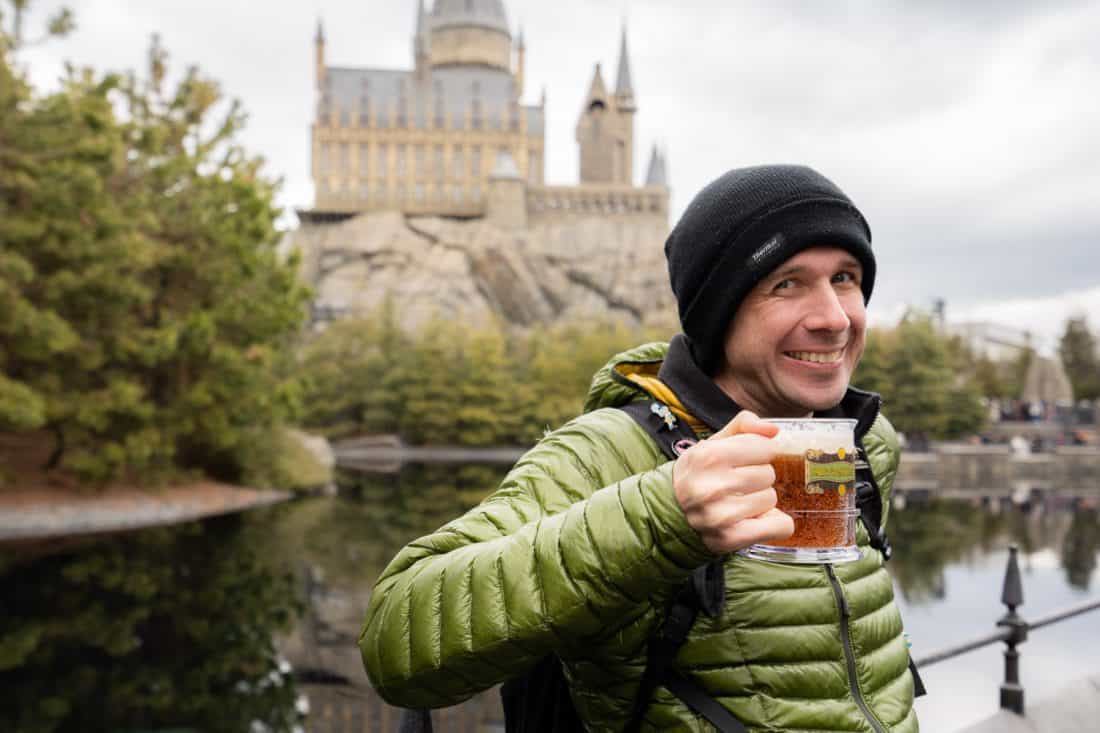 Simon drinking butterbeer on the terrace of the Three Broomsticks with Hogwarts Castle behind him at The Wizarding World of Harry Potter at Universal Studios Japan in Osaka