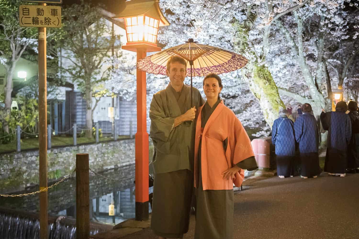 Erin and Simon in winter kimonos by the cherry blossom lined canal at night at Kinosaki Onsen Town, one of the best things to do in Japan