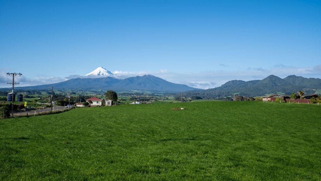 View of snow-capped Mount Taranaki and green farmland while driving around Taranaki region, New Zealand