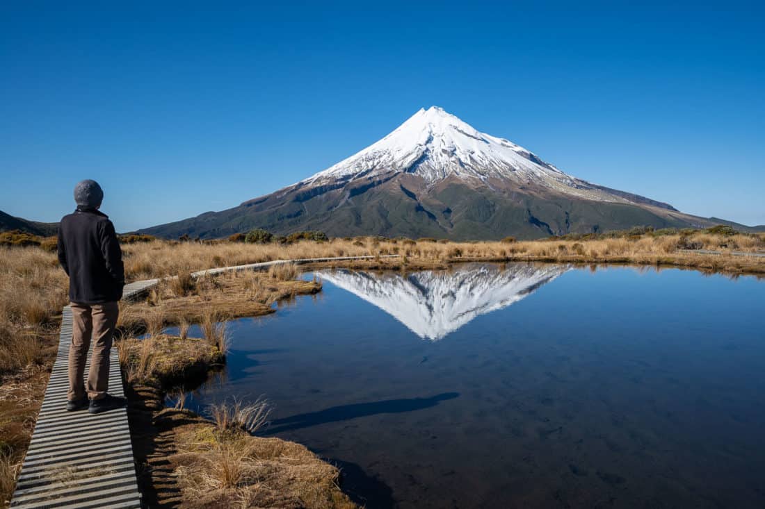 Walking on the boardwalk at Pouakai Tarn with Mt Taranaki reflected in the water on a clear day, New Zealand