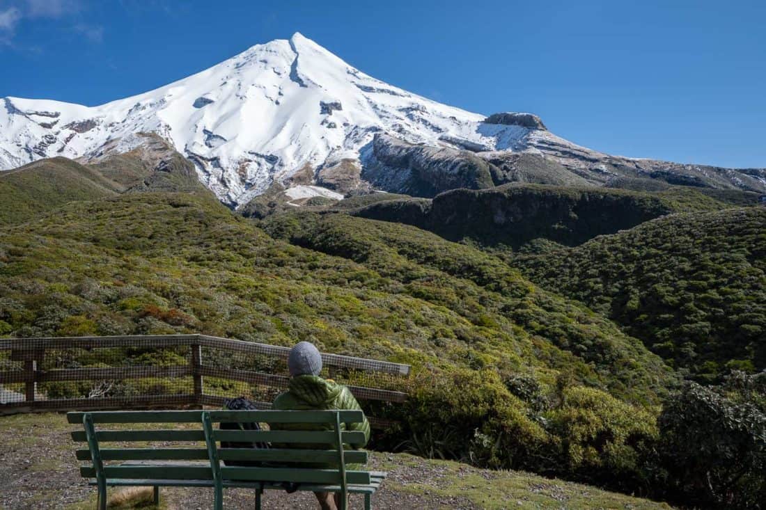 Sitting on a bench at Stratford Plateau with a view of snow-capped Mt Taranaki, New Zealand