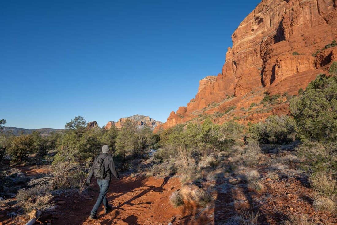 Simon walking towards large red Courthouse Butte in Sedona with clear blue sky and green trees, Arizona, USA