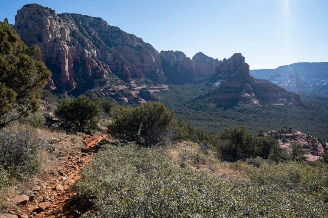 View of craggy mountain range on the Brins Mesa Loop in Sedona with a sloping path and green surroundings