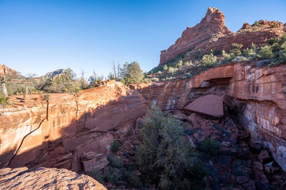 Devil's Kitchen large sinkhole on the Soldier Pass Trail in Sedona with a pink craggy peak in the background and blue sky, Sedona, Arizona, USA