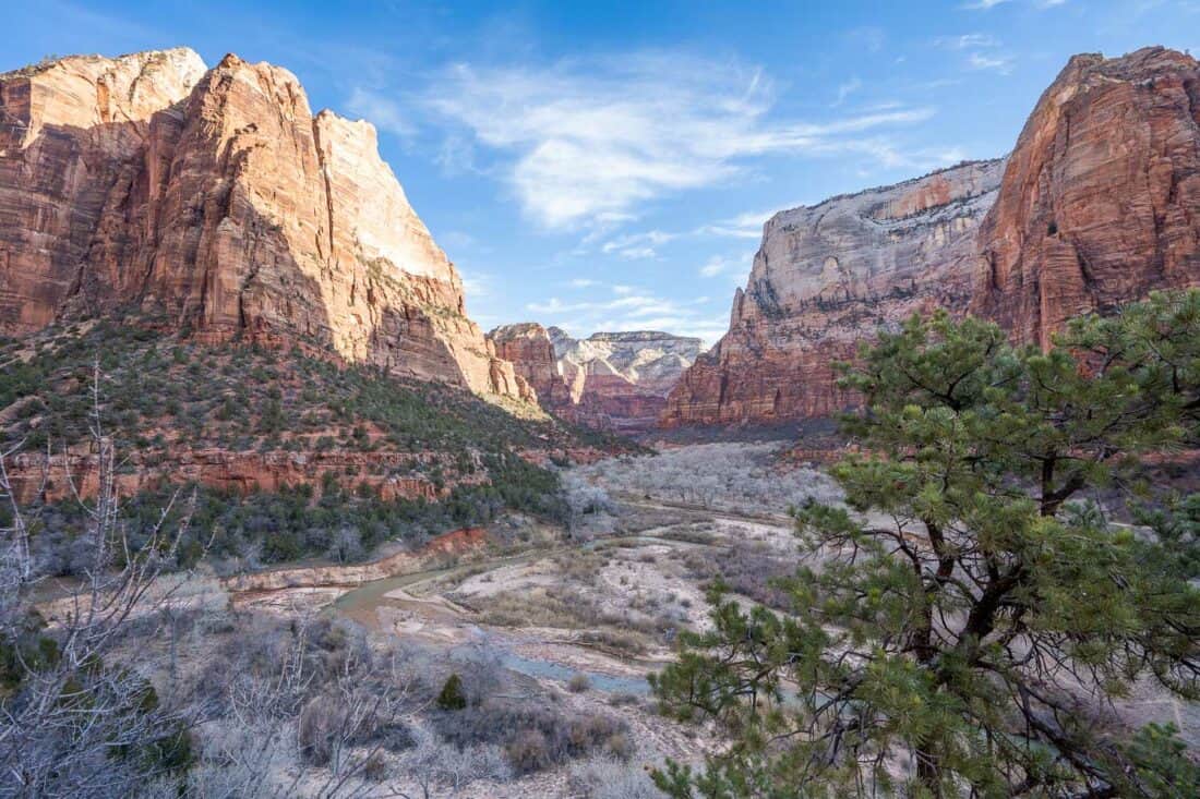 Emerald Pools trail in Utah with pink cliffs partially in shadow, winding stream and blue sky with swirly clouds