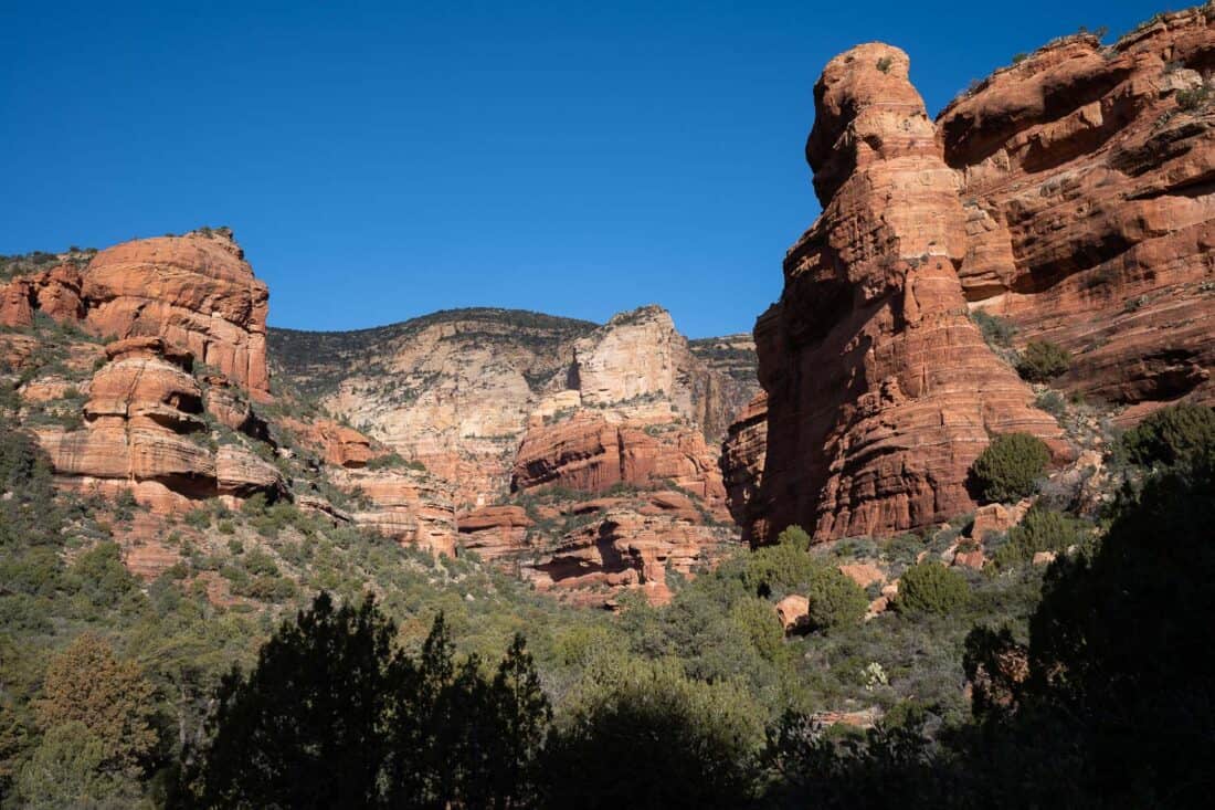 Pink rocky arch formations against a blue sky in Fay Canyon in Sedona with greenery below, Arizona, USA