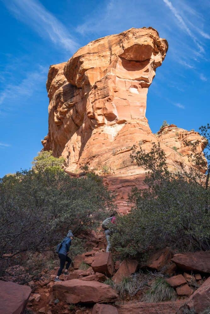 Hikers walking up towards a pink arch formation in Fay Canyon in Sedona, Arizona, USA