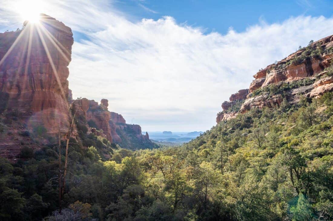 Fay Canyon view in Sedona with a bright sun over red cliffs and green trees and bushes below