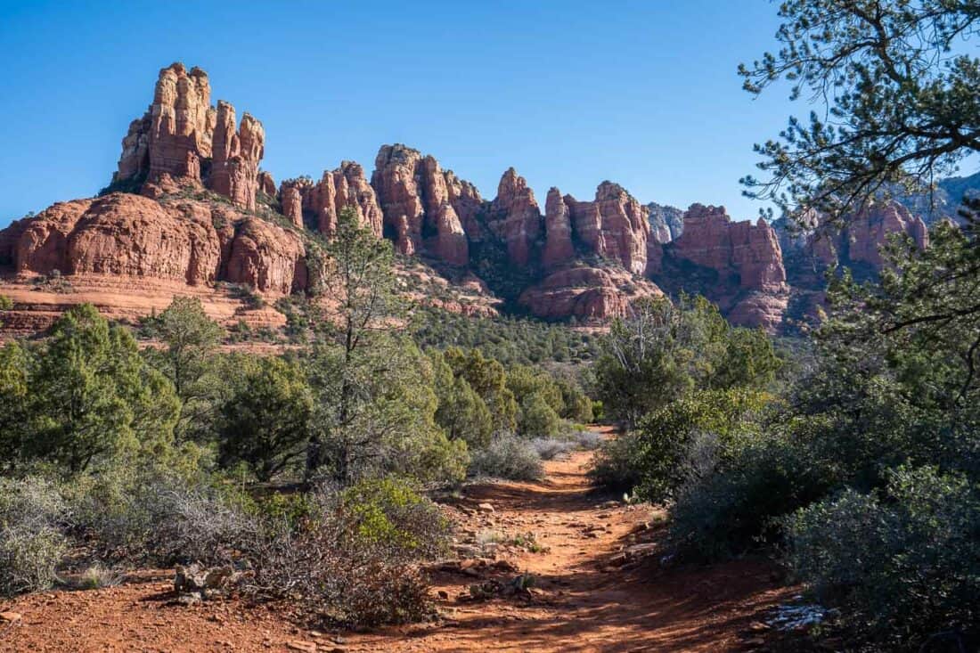 Footpath to red craggy Snoopy Rock on the Margs Draw Trail in Sedona with green juniper trees, Arizona, USA