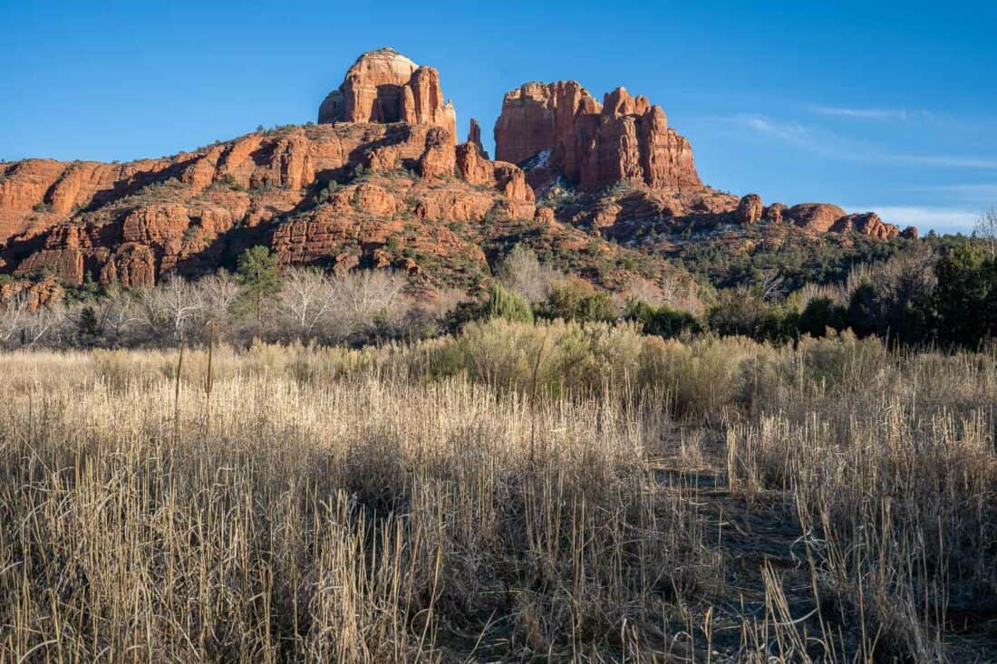 Towering Cathedral Rock in Sedona against a blue sky and green meadow