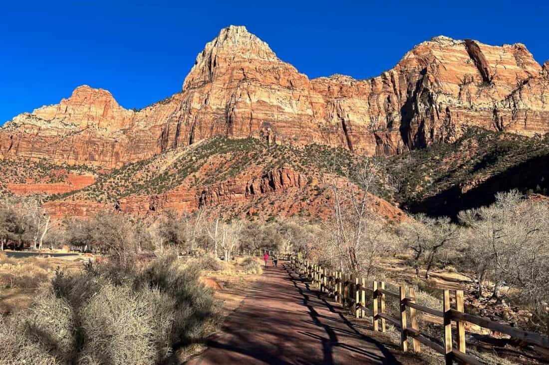 People walking along the paved Pa'rus Trail with a backdrop of pink cliffs and clear blue sky in Zion National Park, Utah, USA