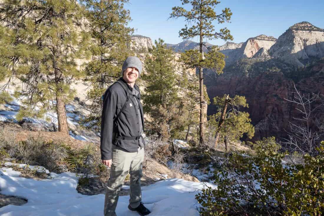 Simon dressed warmly with a beanie hat hiking in the snow surrounded by trees in Zion National Park, Utah, USA