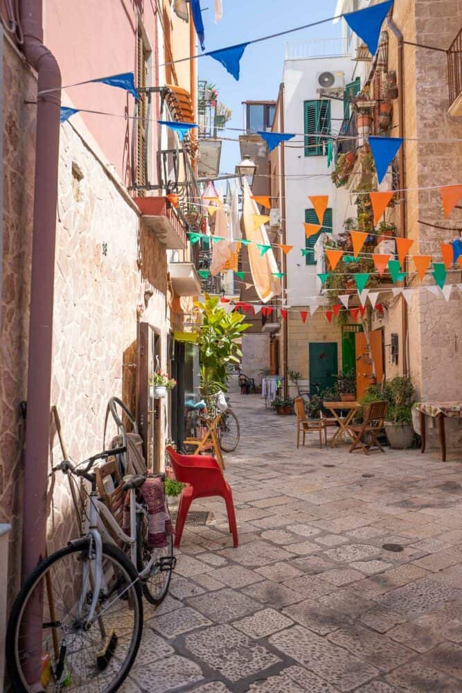 Bike leaning against a wall in a narrow lane in Bari Vecchia with colourful bunting strewn above seating