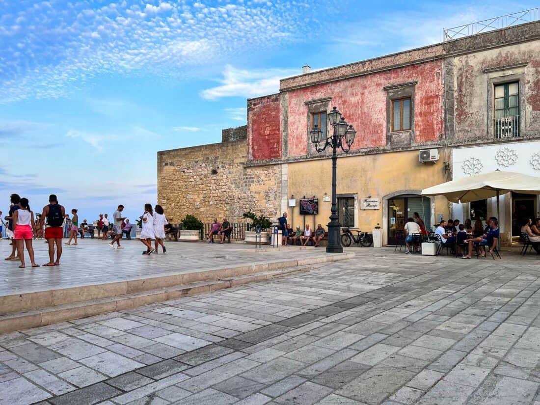 People enjoying Belvedere di Castro lined with rustic faded buildings. Castro, Italy