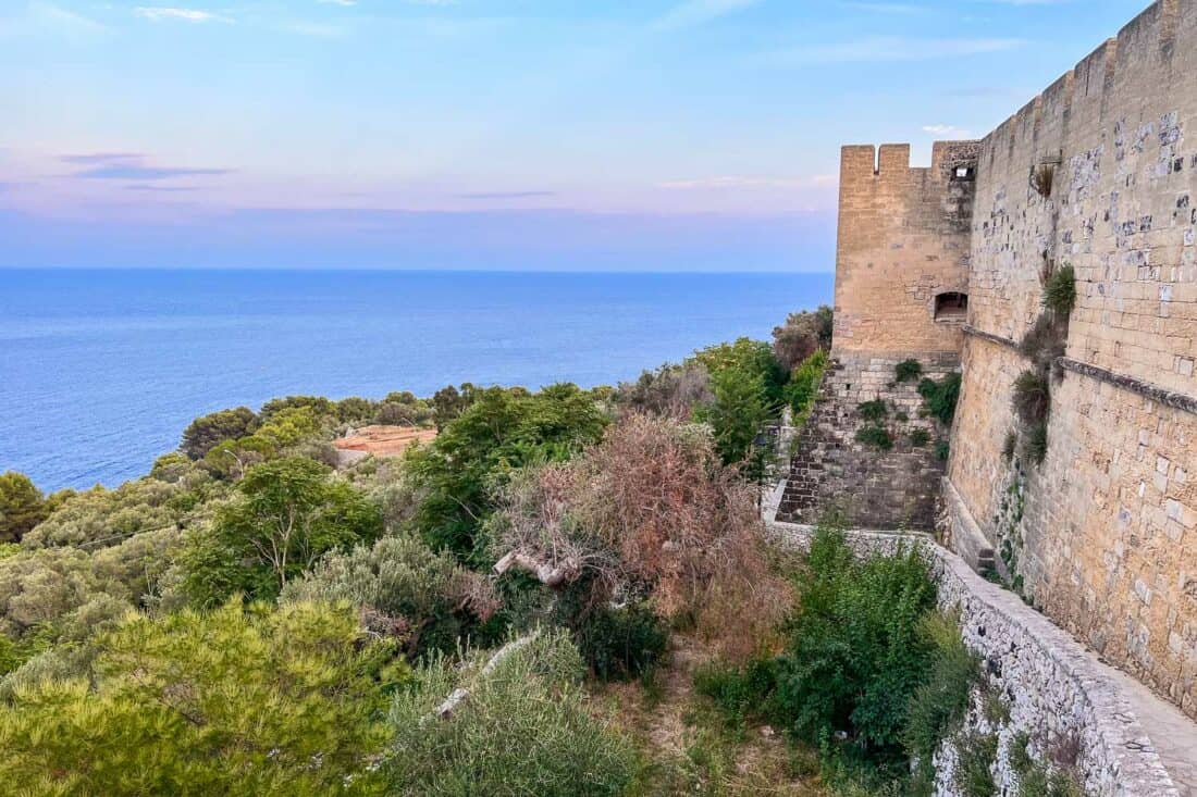 City wall path along Castello Aragonese overlooking the sea and trees at dusk, Castro, Italy