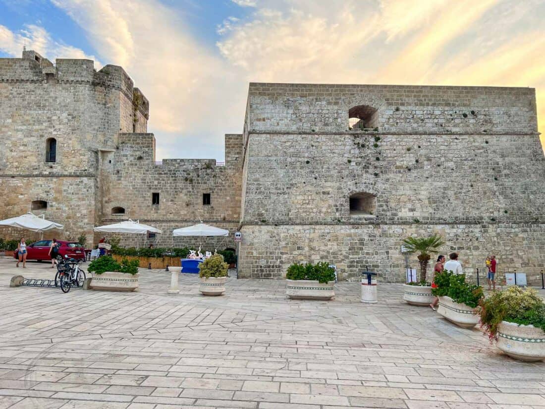 Exterior stone facade of Castello Aragonese with large potted plants lining the piazza, Castro, Italy