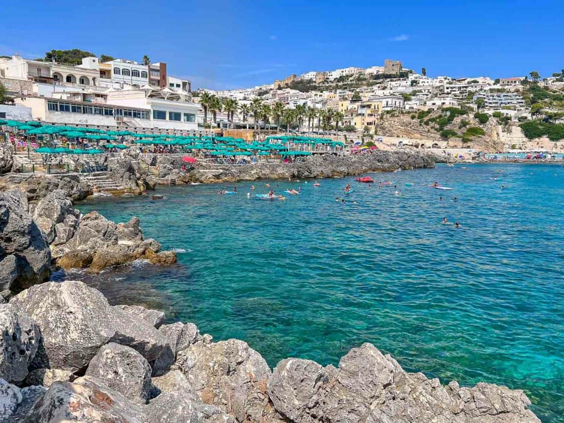 People swimming in aquamarine waters in Castro surrounded by a rocky harbour overlooked by a resort