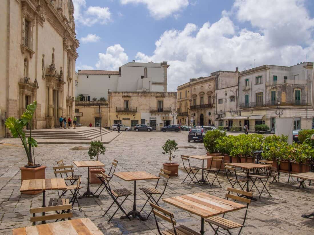 Tables and chairs in a quiet piazza with a church and potted plants in Galatina, Salento