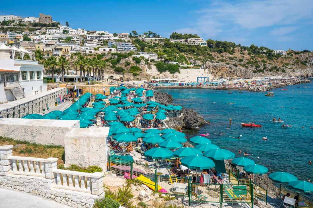 Turqoise parasols by the sea at Lido La Sorgente, overlooked by Castro old town on the hillside, Puglia