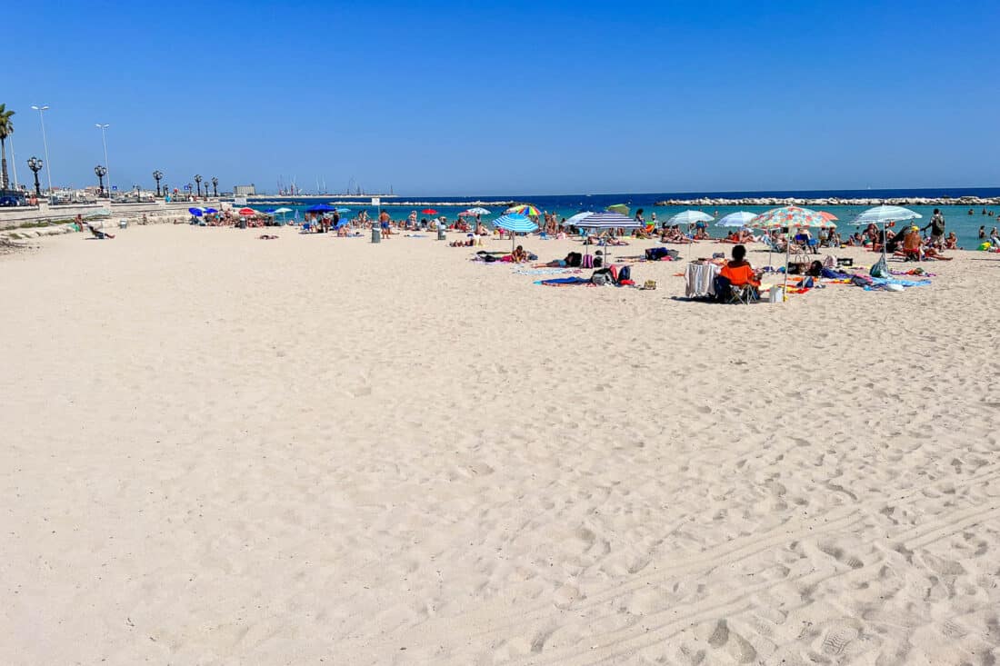 People relaxing on the white sandy Pane e Pomodoro beach in Bari with a clear blue sky above, Puglia, Italy