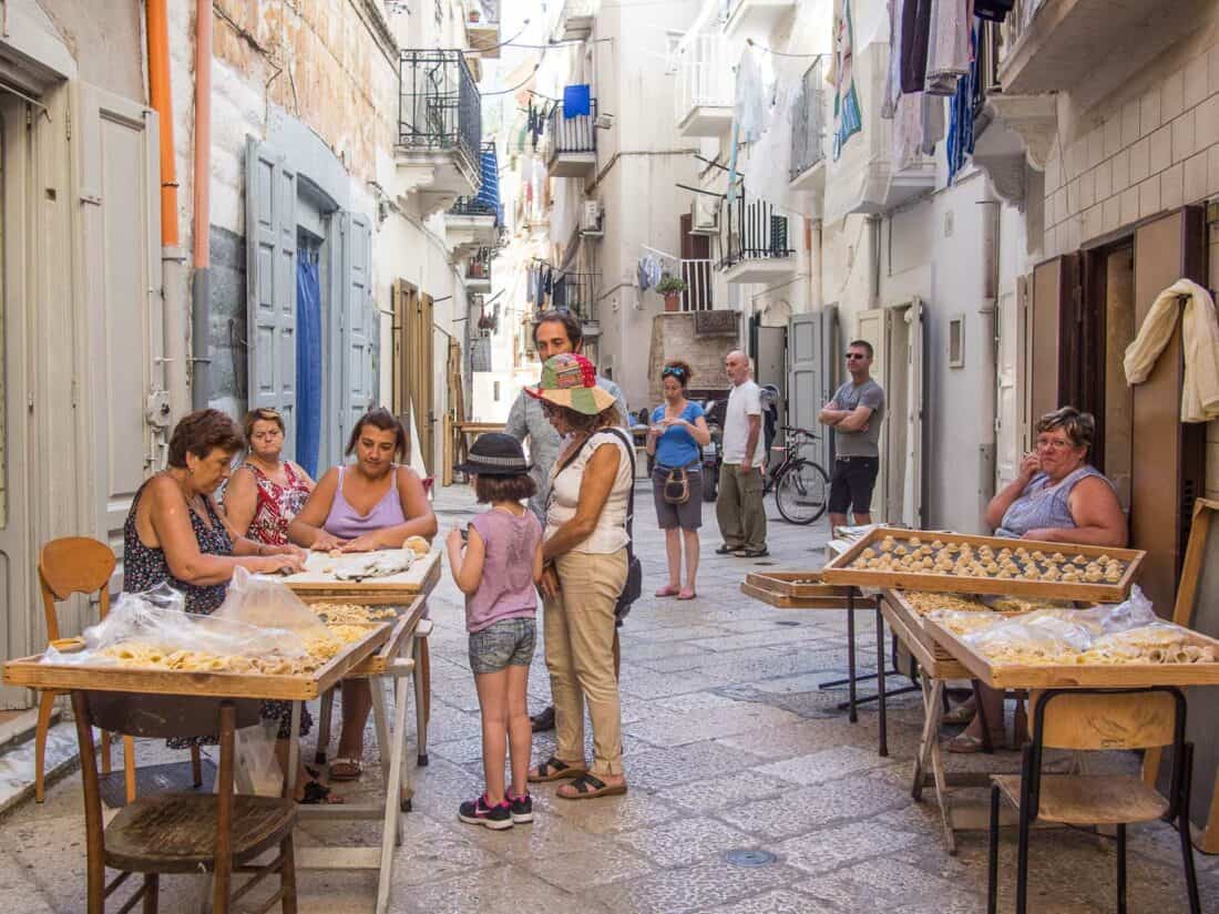 Local women making and selling fresh pasta from tables in a narrow alley in Bari, Italy