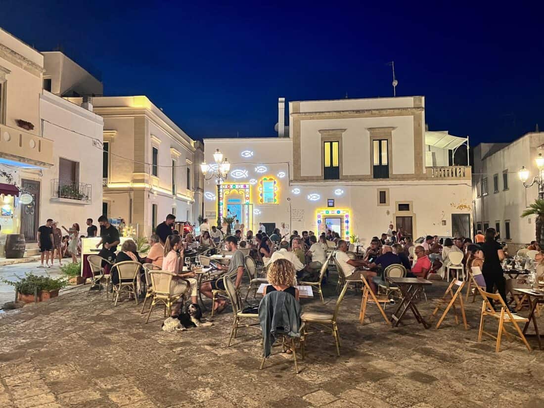 People dining in Piazza della Vittoria decorated with lights at night time, Castro, Italy