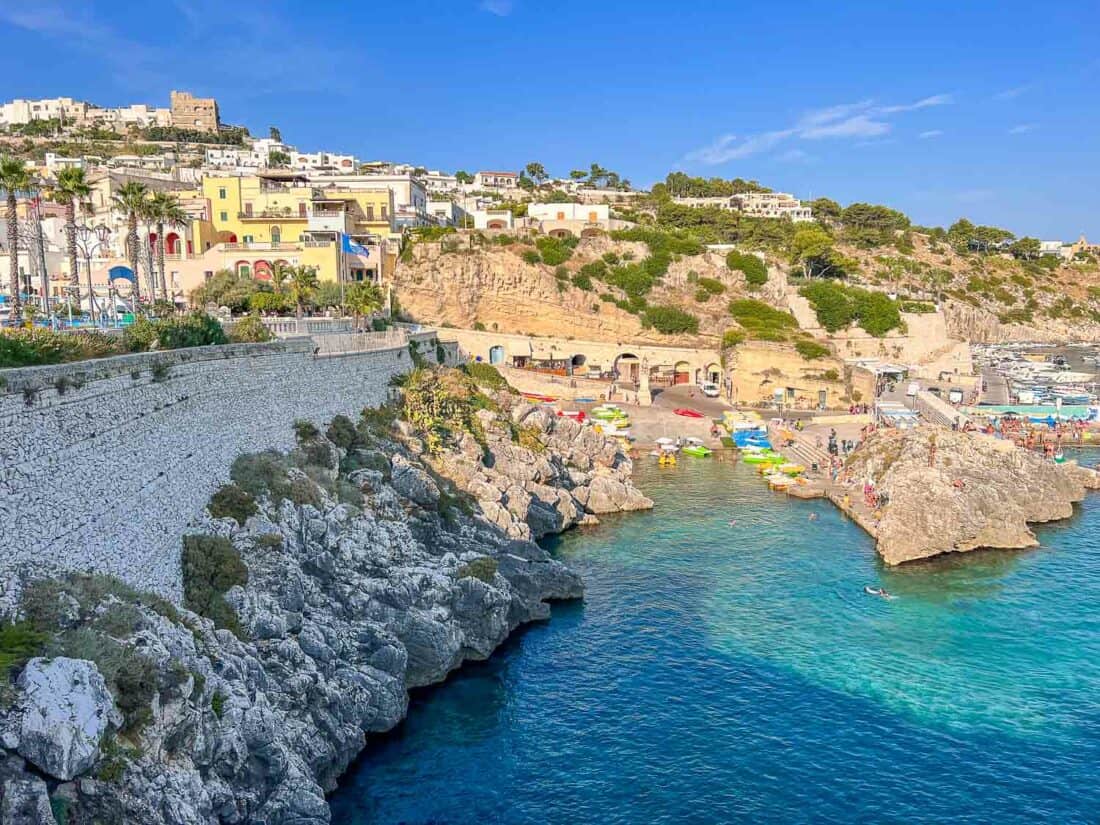 Cliffs and city walls leading down to Castro port with boats docked on a sunny day, Castro, Italy