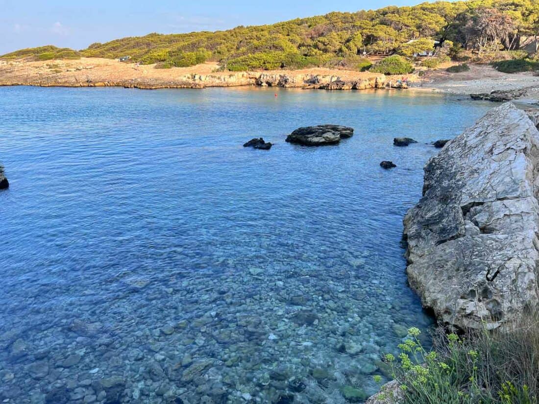 Crystal clear blue water at Porto Selvaggio beach, Italy with a backdrop of green woods