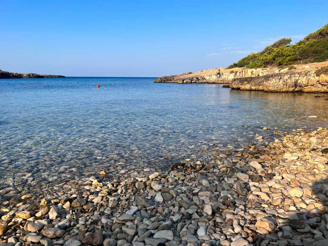 Pebbly Porto Selvaggio beach with clear blue waters on a sunny morning, Italy