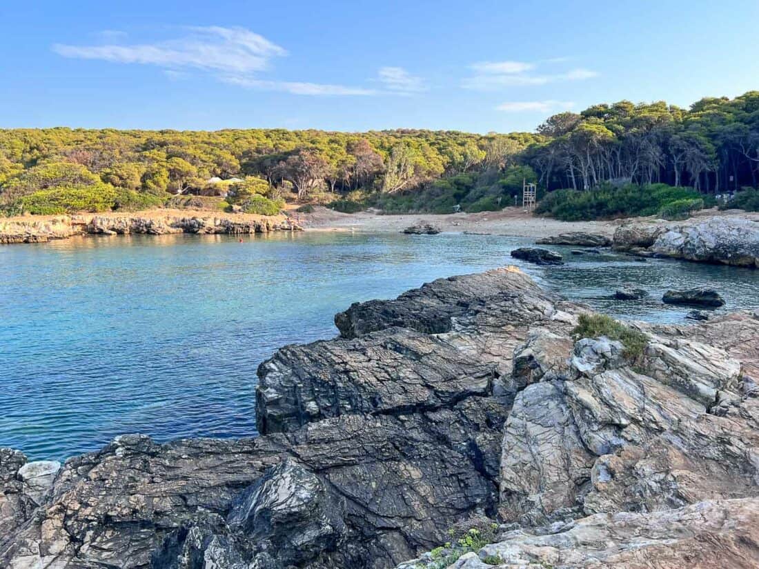 Beach at Porto Selvaggio surrounded by rocky shores and lush green woodland, Salento