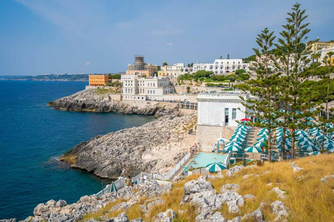 Cliffside view of Santa Cesarea Terme's thermal sulphur pool with parasols and tall trees, Salento, Italy