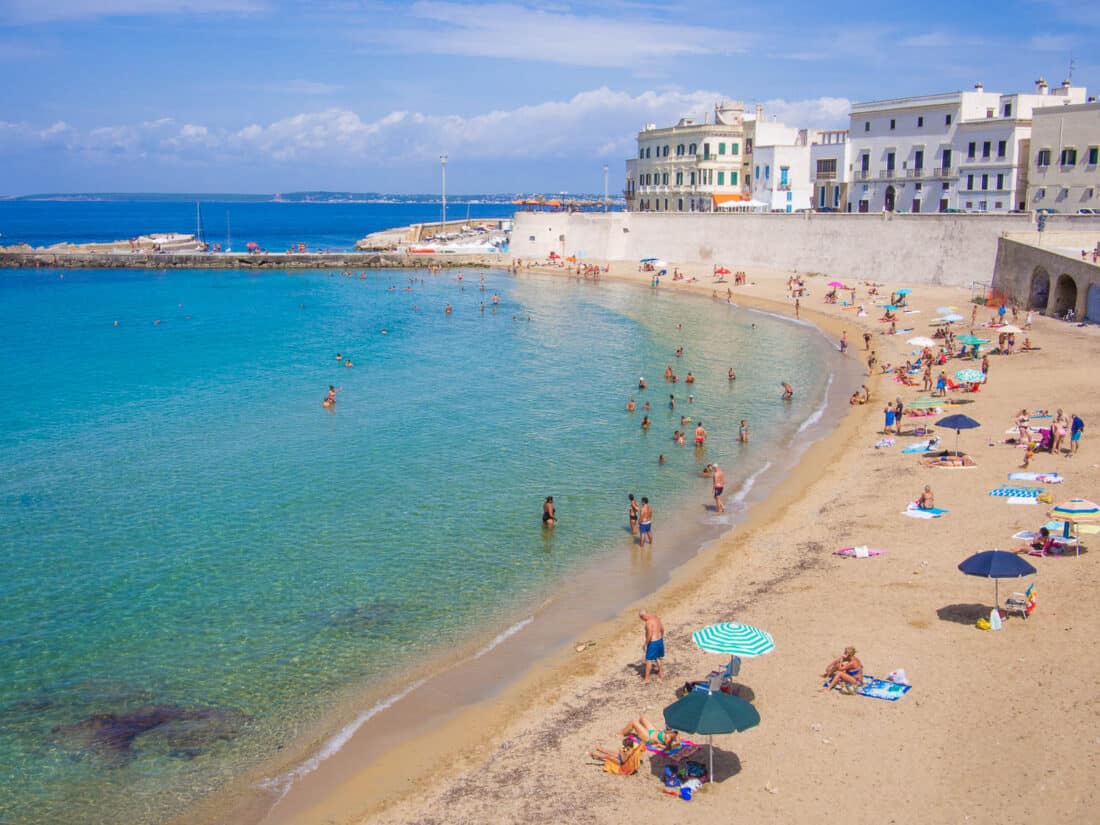 People relaxing on the beach in Gallipoli overlooked by the city walls and white buildings, Puglia, Italy