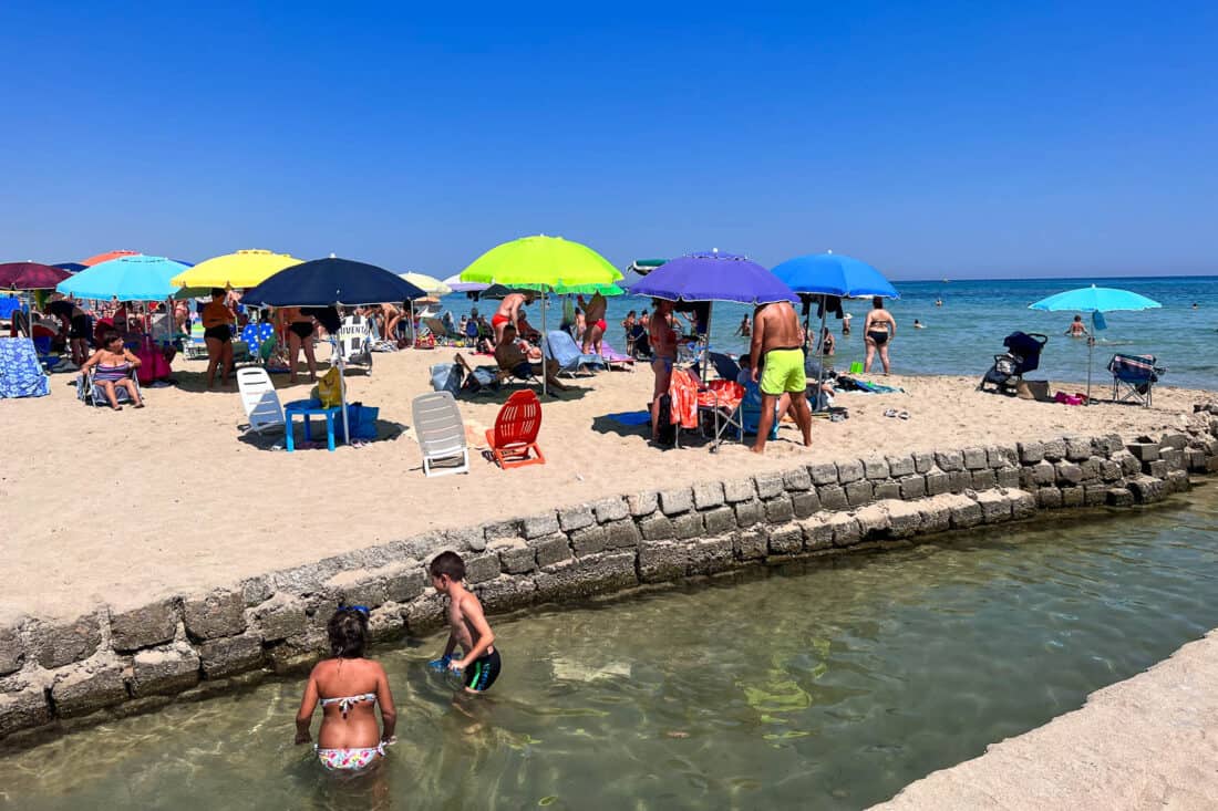 People sunbathing and children playing on the busy Lido Morelli Beach in summertime, Puglia