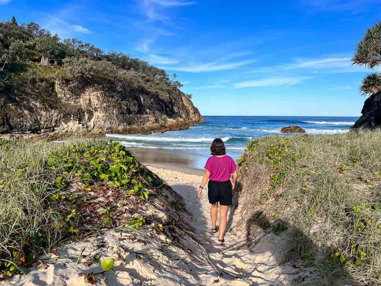 Erin walking towards the tiny cove of South Gorge Beach with white sands on a blue sky day, North Stradbroke Island, Queensland, Australia