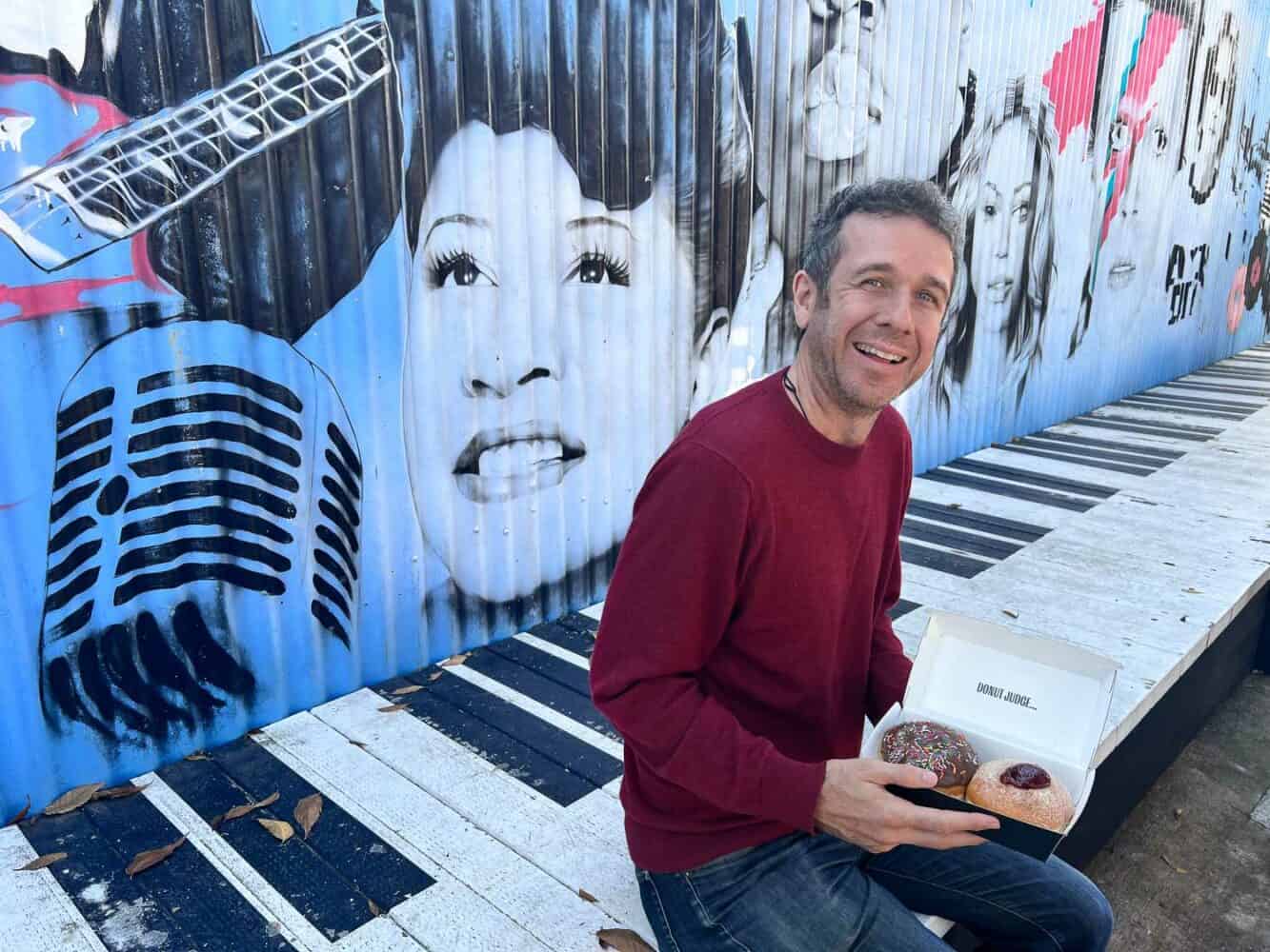 Simon enjoying his Kenilworth Bakery donuts with a colourful mural behind him, Sunshine Coast Hinterland, Queensland, Australia