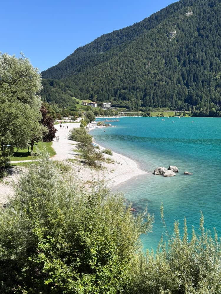 Beach in Molveno with white pebbles and clear turquoise water.