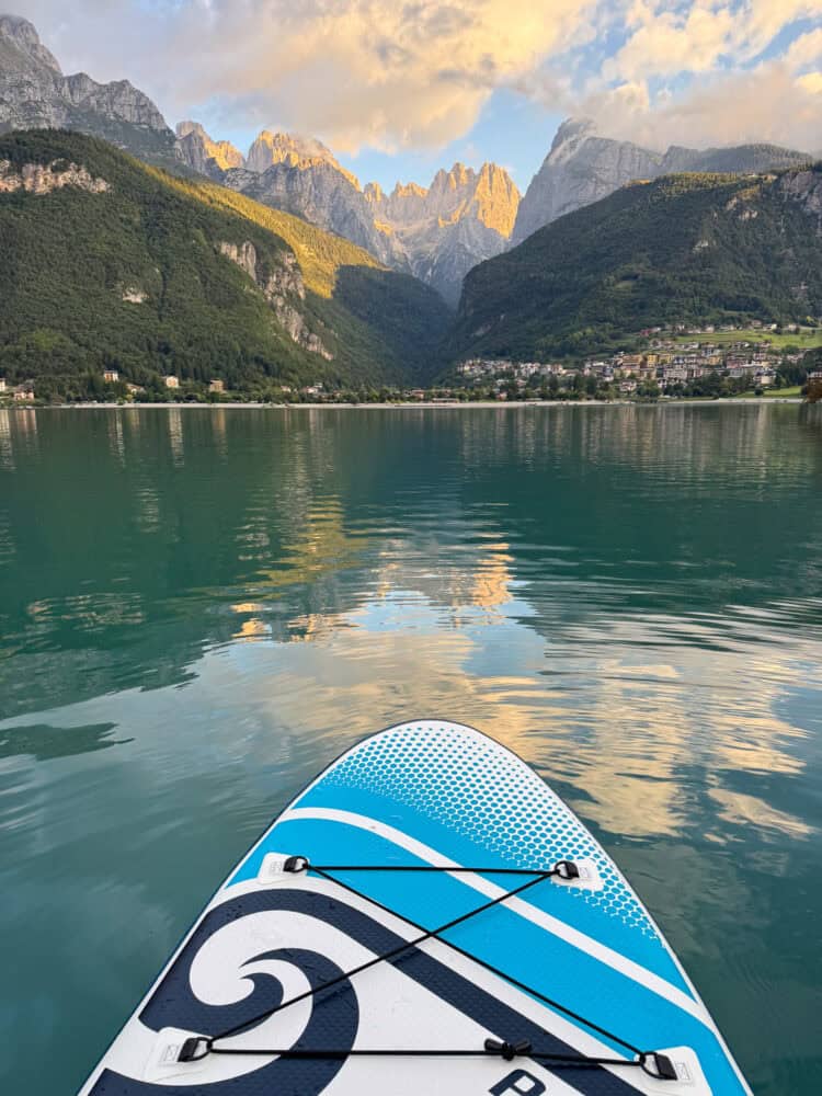 Paddleboarding on Lake Molveno at sunrise with the mountains glowing orange and reflected in the water.