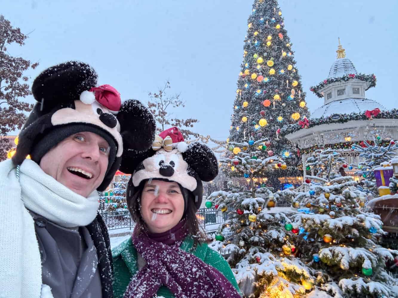 Simon and Erin in the snow at Disneyland Paris at Christmas with the Christmas Tree in the background.
